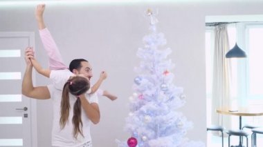 Güçlü yakışıklı baba kızını omuzlarına alır, kızı gösteri yapar ve yılbaşı ağacındaki toplardan birini kaldırır..