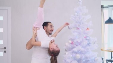 Oyuncu baba ve atletik kızı, babasının omuzlarında ayrı pozisyonda, köknar ağacını birlikte süslüyorlar..