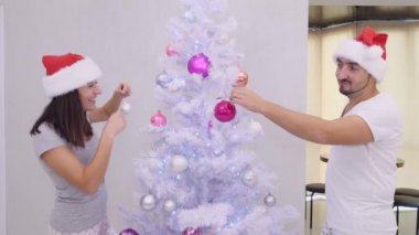Gümüş Noel ağacının farklı taraflarında duran komik eş ve koca, etrafta dolanıp süsleniyorlar, güzel Noel Baba şapkaları giyiyorlar..