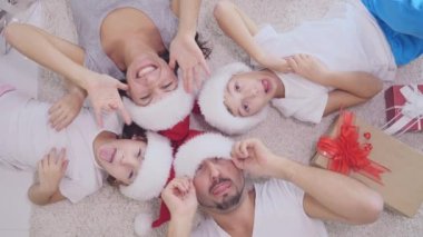 Yaratıcı ve komik bir aile, tepeden tırnağa halıya uzanmış güneş yapıyor, farklı suratlarla kameraya bakıyor..