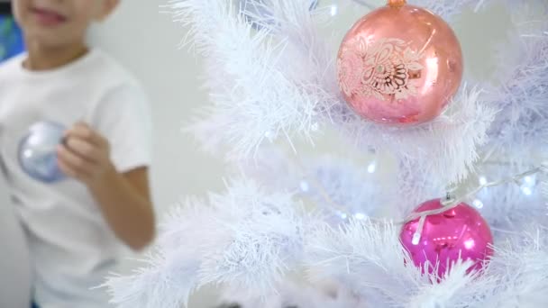 Argent sapin de Noël avec des boules à l'avant-plan et enfant flou sur le fond accrochant la boule de verre argent — Video