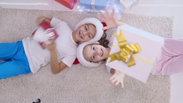 Gelukkige kinderen liggen op het tapijt en gooien kerstdozen, genieten van zorgeloze tijd. — Stockvideo
