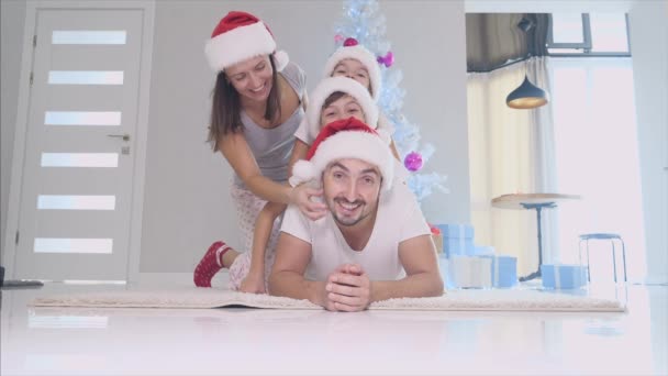 Twee broers en zussen en ouders rotzooien, vader zwaait op het tapijt, zoon op de vaders terug, dochter op de broers terug, moeder is bij hen, glimlachend. — Stockvideo