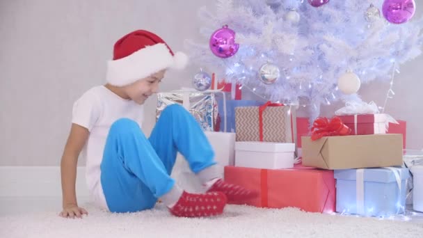 Sabırsız küçük çocuk geceleri gizlice Noel ağacına gider, kimse bir hediye kutusunu görüp açtığında, tamamen şaşırmış bir şekilde içine bakar, sonra da ağacın altına geri koyar.. — Stok video