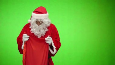 Noel Baba yeşil arka planda hediyelerle dolu bir çantaya bakar.
