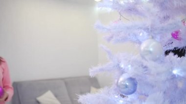 Noel ağacını süslemekten mutluluk duyan, Noel ruhunun tadını çıkaran güzel bir genç kadının 4K videosu..