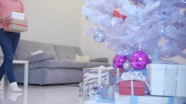 Noel Baba rolünde gülümseyen beyaz kadın Noel ağacının altına yılbaşı hediyesi koyuyor..