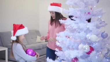 Küçük kızı bir sürü pembe cam takı taşıyor, annesi mücevherleri alıyor ve bir köknar ağacı süslüyor..