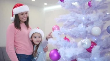 Anne ve kızı, Noel ağacının yanında duran tatlı kız köknar dalındaki pembe takılardan birini işaret ediyor..