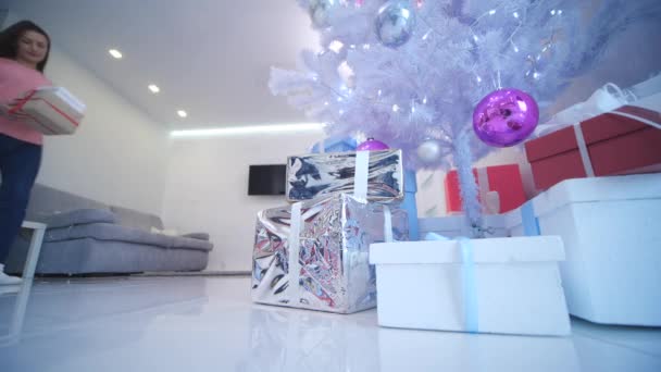 Aandachtige moeder bereidt cadeautjes voor kinderen op wintervakantie, waardoor ze onder de eerste boom. — Stockvideo