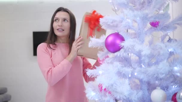 Linda madre con un regalo de Navidad en la mano, caja de espera cerca de la oreja, temblando y escuchando lo que hay dentro . — Vídeos de Stock