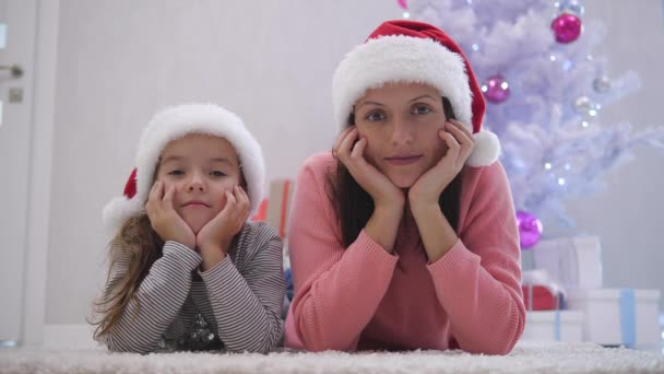 Closeup video of young mother and daughter lying on the carpet near fir-tree, enjoying time together. — Stock Video