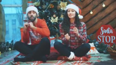 Havalı, eğlenceli, eğlenceli partnerler örgülü kırmızı elbiseler ve Noel Baba şapkaları giyiyorlar etrafta oynuyorlar, dans ediyorlar, loto pozisyonunda oturuyorlar..