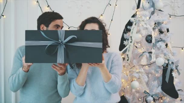Αγόρι και κορίτσι κρατώντας τεράστιο γκρι κουτί δώρου με ριγέ σερπαντίνες, και κάνοντας γκριμάτσες. — Αρχείο Βίντεο