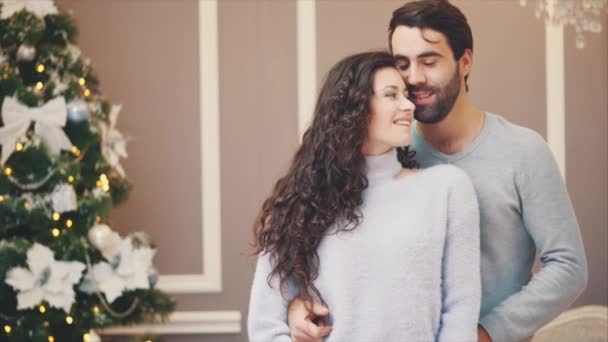 Speranzoso uomo e donna in piedi vicino all'albero di Natale, la donna stende un regalo legato con un nastro rosso, guardando la macchina fotografica sorridente. . — Video Stock