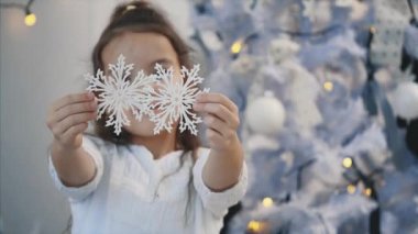 Küçük kız evde gümüş kar taneleriyle bir Noel ağacı süslüyor ve onları kameraya gösteriyor..