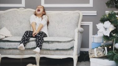 Çocuk Noel ağacının yanındaki kanepede uyuyakalır ve sabah uyanır ve hediye kutularını açar..