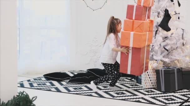 La niña cariñosa lleva una pila de cajas de regalos para sus amigos y familiares al árbol de Navidad . — Vídeo de stock