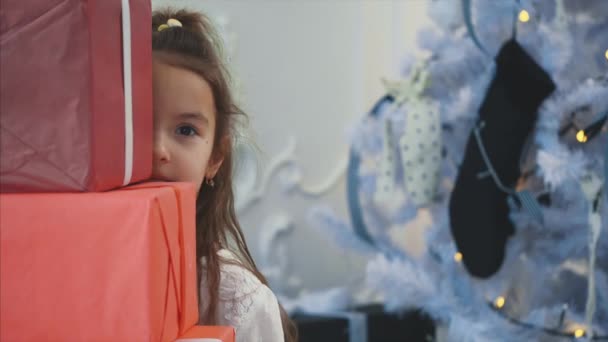 Nahaufnahme 4k Video von charmanten Mädchen, die hinter einem Stapel von Geschenkboxen hervorlugen, winkende Hand, Gruß an alle anlässlich des neuen Jahres, alles Gute wünschend. — Stockvideo