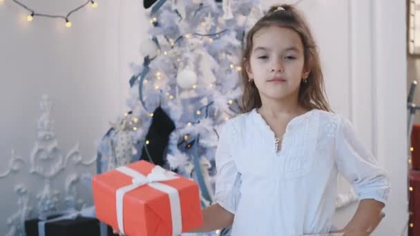 Close-up Kaukasisch meisje presenteert een geschenk in een rode doos, poseren, het houden van een hand akimbo, op zoek naar vertrouwen. — Stockvideo