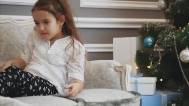 Çocuk Noel ağacının yanındaki kanepede uyuyakalır ve sabah uyanır ve hediye kutularını açar..