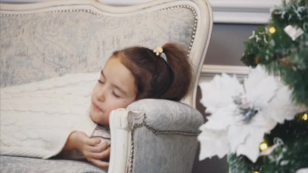 Closeup video of daughter falling asleep on the sofa near Christmas tree to wake up in the morning and unpack giftboxes. — Stock videók