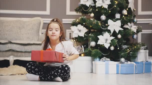 Рекламне відео, де маленька дівчинка отримала подарункову коробку і презентує її перед камерою на різдвяному тлі . — стокове відео