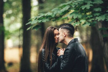 Bir kadının ellerini ısıtan şefkatli bir adam, sonbahar parkının bulanık arka planında burunlarına dokunurken onları ovuyor..