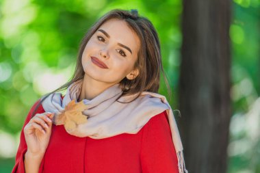 Güz yaprağını tutan sevimli esmer kızın görüntüsü. Masum ve samimi bir şekilde bulanık park geçmişine bakıyor..