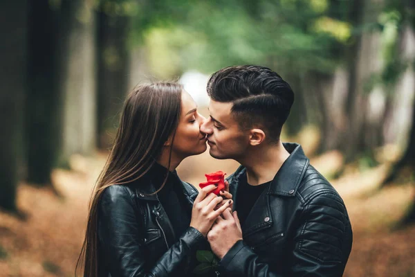 Namiętny młody mężczyzna i kobieta całujący się w jesiennym parku, trzymający czerwoną różę. — Zdjęcie stockowe