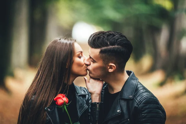 在金娘日落时分，红玫瑰的快乐女孩在公园散步时亲吻着她的男朋友. — 图库照片