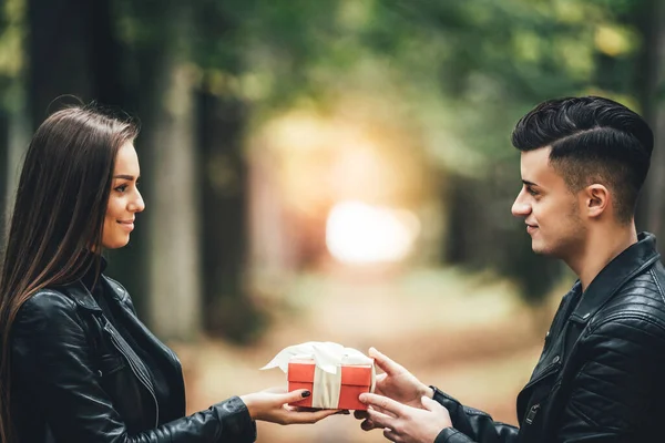 Homem atento dá a sua namorada um presente amarrado com fita branca sobre fundo de outono borrado . — Fotografia de Stock