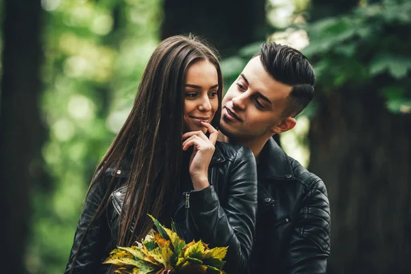 Hübsches Paar umarmt und flirtet im Stadtpark, Frau hält einen Strauß Herbstblätter in der Hand und hört ihrem Mann zu. — Stockfoto