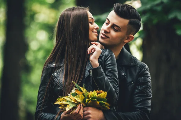 Hübsches Paar umarmt und flirtet im Stadtpark, Frau hält einen Strauß Herbstblätter in der Hand und hört ihrem Mann zu. — Stockfoto