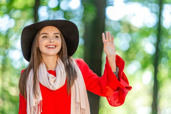 Foto seorang gadis muda lucu yang bahagia di taman kota melambaikan tangan kepada teman-teman halo atau selamat tinggal. — Stok Foto