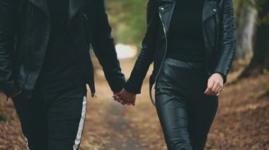 Sonbahar parkında tanınmayan bir çift yürüyor. Tamamen siyah görünüş. Arka plan bulanık. Ekin. Uzayı kopyala 4K.