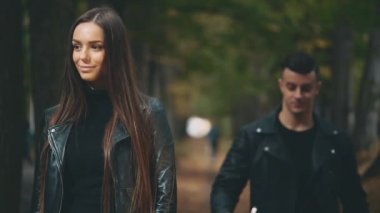 Siyah deri ceketli esmer kız erkek arkadaşını bekliyor. Siyah görünüşlü çocuk kız arkadaşının gözlerini kapıyor ve kırmızı bir gül veriyor. Arka plan bulanık. Uzayı kopyala 4K.