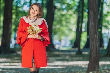 Yüzü rüya gibi olan gülümseyen kız bir demet düşmüş akçaağaç sarısı yaprağı tutuyor. Sonbahar buket konsepti.