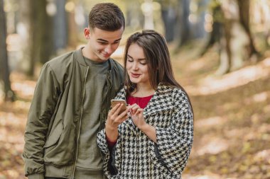 Boş zaman ve teknoloji konsepti. Akıllı telefonlu gülümseyen arkadaşlar parkta dikilip birlikte medyayı izliyorlar..