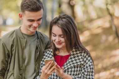 Boş zaman ve teknoloji konsepti. Akıllı telefonlu gülümseyen arkadaşlar parkta dikilip birlikte medyayı izliyorlar..