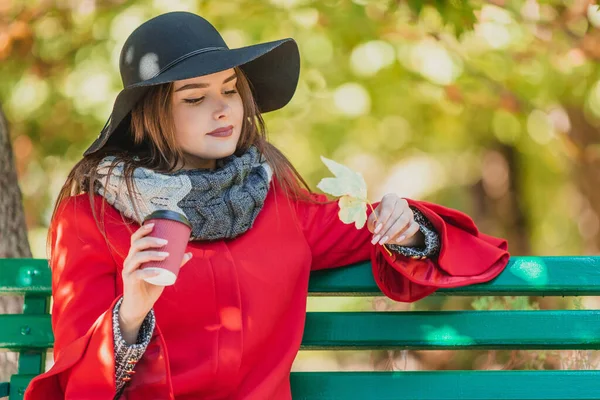 Wanita jatuh minum kopi di taman kota musim gugur, menikmati daun kuning yang indah dan kedamaian musim gugur. — Stok Foto