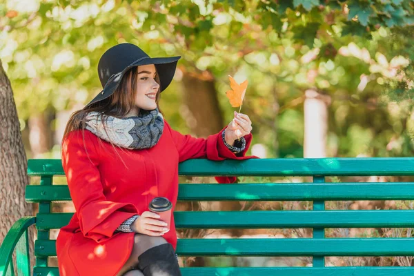 Sonbahar kadını sonbahar parkında kahve içiyor, güzel sarı yaprakların ve sonbaharın huzurunun tadını çıkarıyor..
