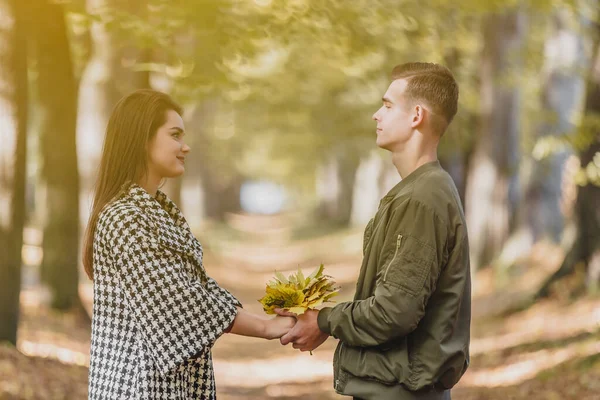 Igaz szerelem. Gyönyörű fiatal pár kezében egy köteg levél, és tartsa a szemkontaktust a napsütéses őszi napon a parkban. — Stock Fotó