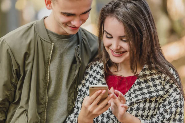 Cropped photo of cheerful girl, showing photos to her boyfriend, while they are spending free time in autumn park. — Stock Photo, Image