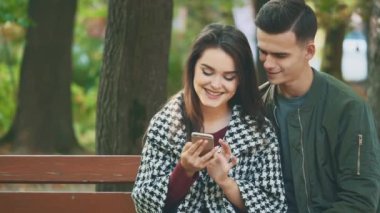 Çift birlikte akıllı telefona bakıyor, parkta bir bankta oturuyor. 4K.