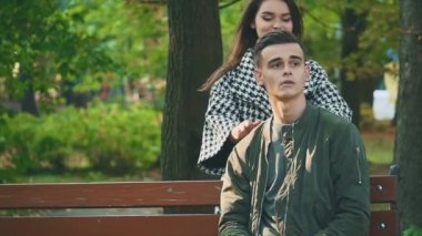 Genç adam sevgilisini bekliyor, bankta oturuyor, sonbaharın bulanık arka planında. Kapatın. 4K.