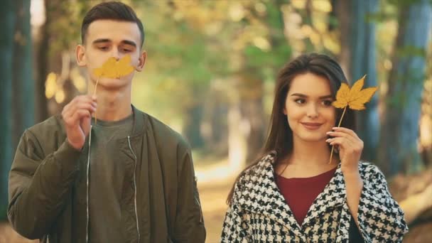 Heureux couple caucasien souriant imite feuille jaune pour être leurs yeux, sur fond de parc flou. Ferme là. Espace de copie. — Video