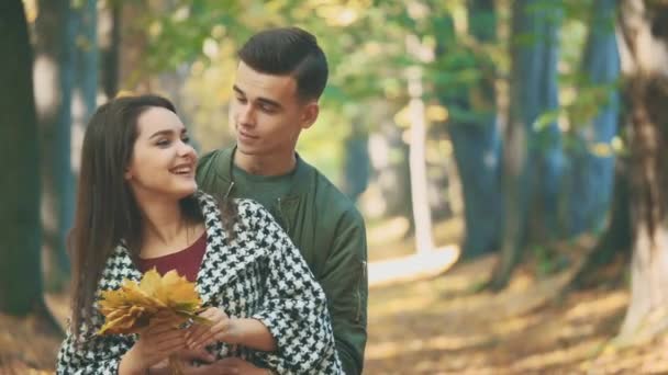 El chico está abrazando a su encantadora novia. Ella sostiene un montón de hojas de otoño. Fondo borroso. De cerca. Copiar espacio. 4K . — Vídeos de Stock