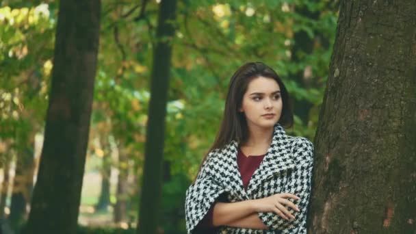 Joven, adorable chica está esperando a su novio cerca de un árbol, estar en un fondo borroso otoño. Guy la está abrazando firmemente. De cerca. 4K . — Vídeo de stock