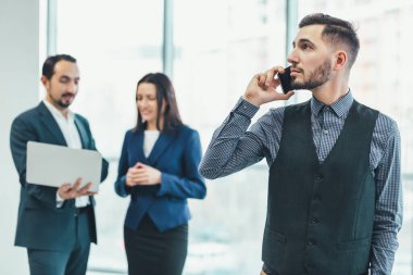 İki iş arkadaşı arka planda tartışırken genç işadamı telefonda konuşuyor ve gözlerini kaçırıyor..